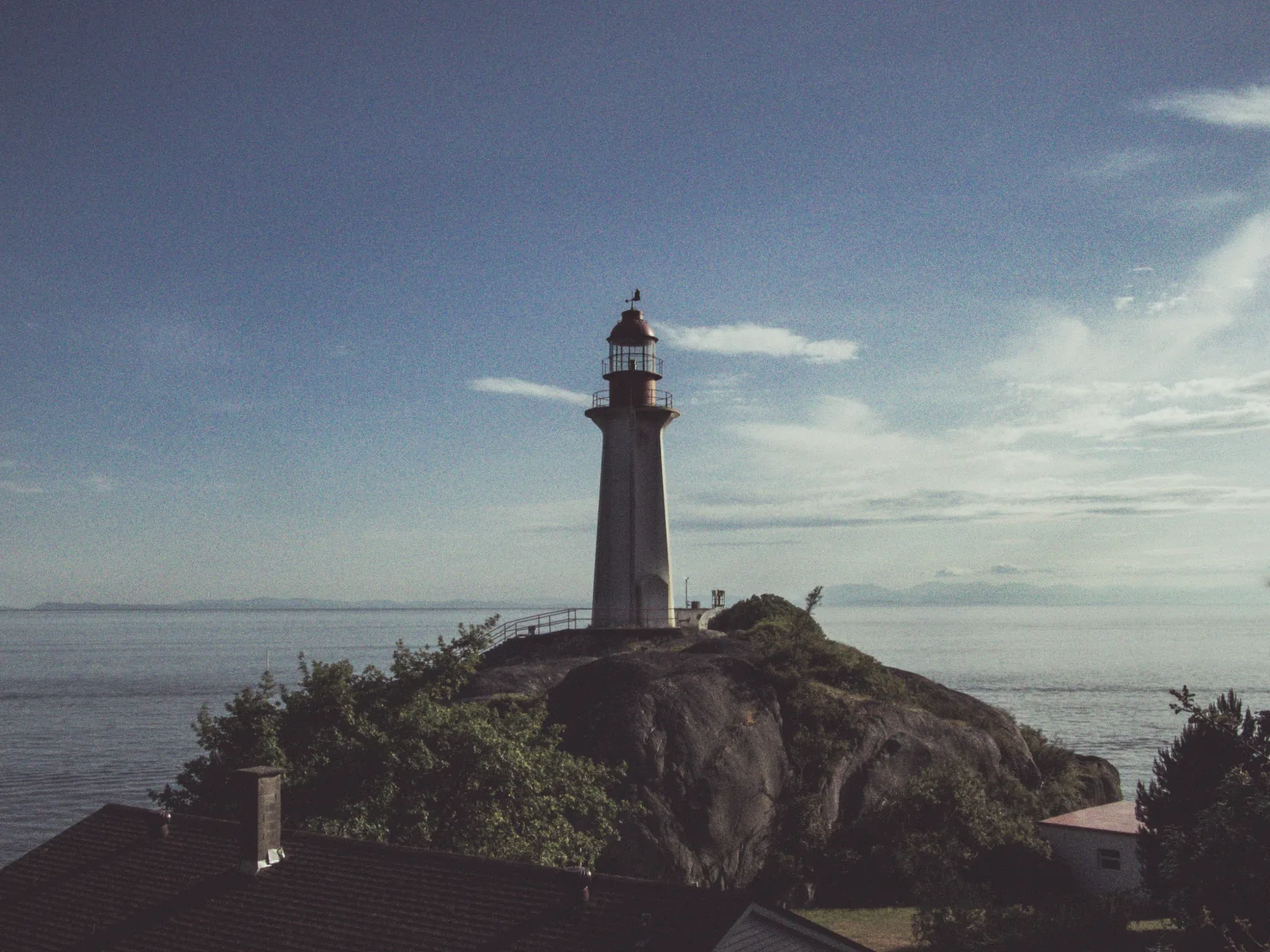 The lighthouse at Lighthouse Park on its rock above the water, open strait behind it on a clear day.
